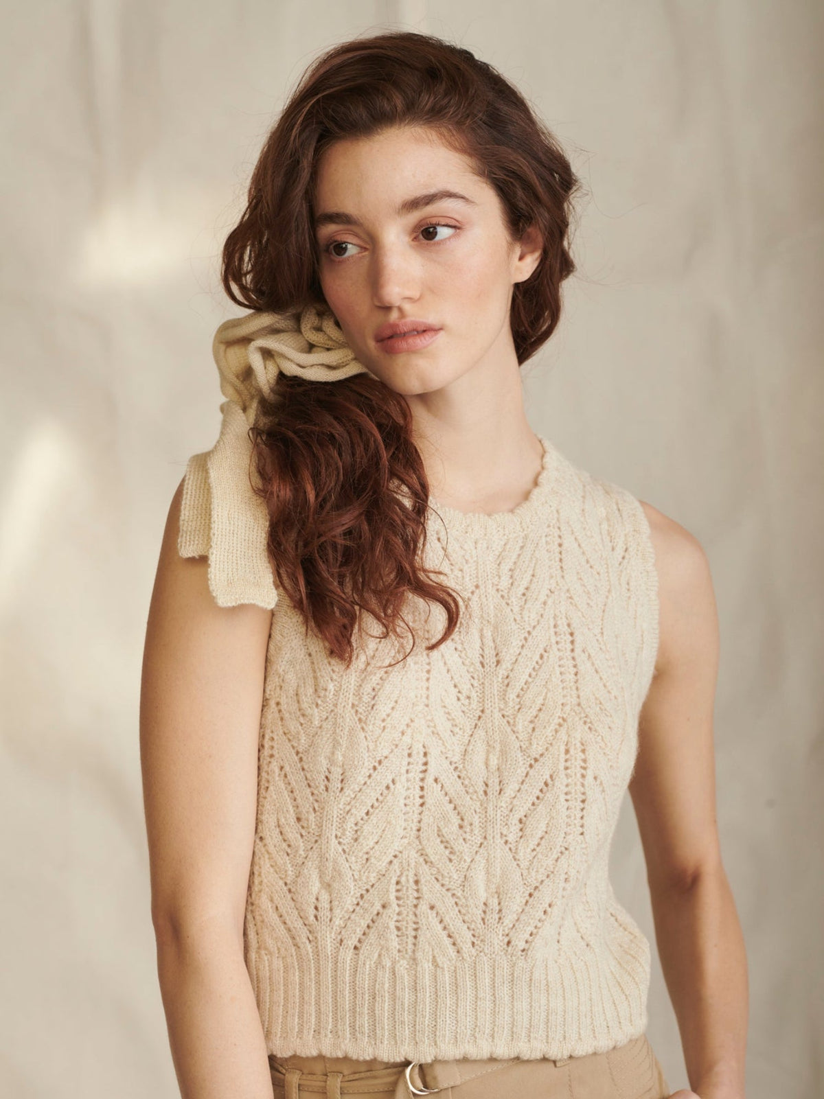 Woman wearing a beige knitted sleeveless sweater against a neutral background