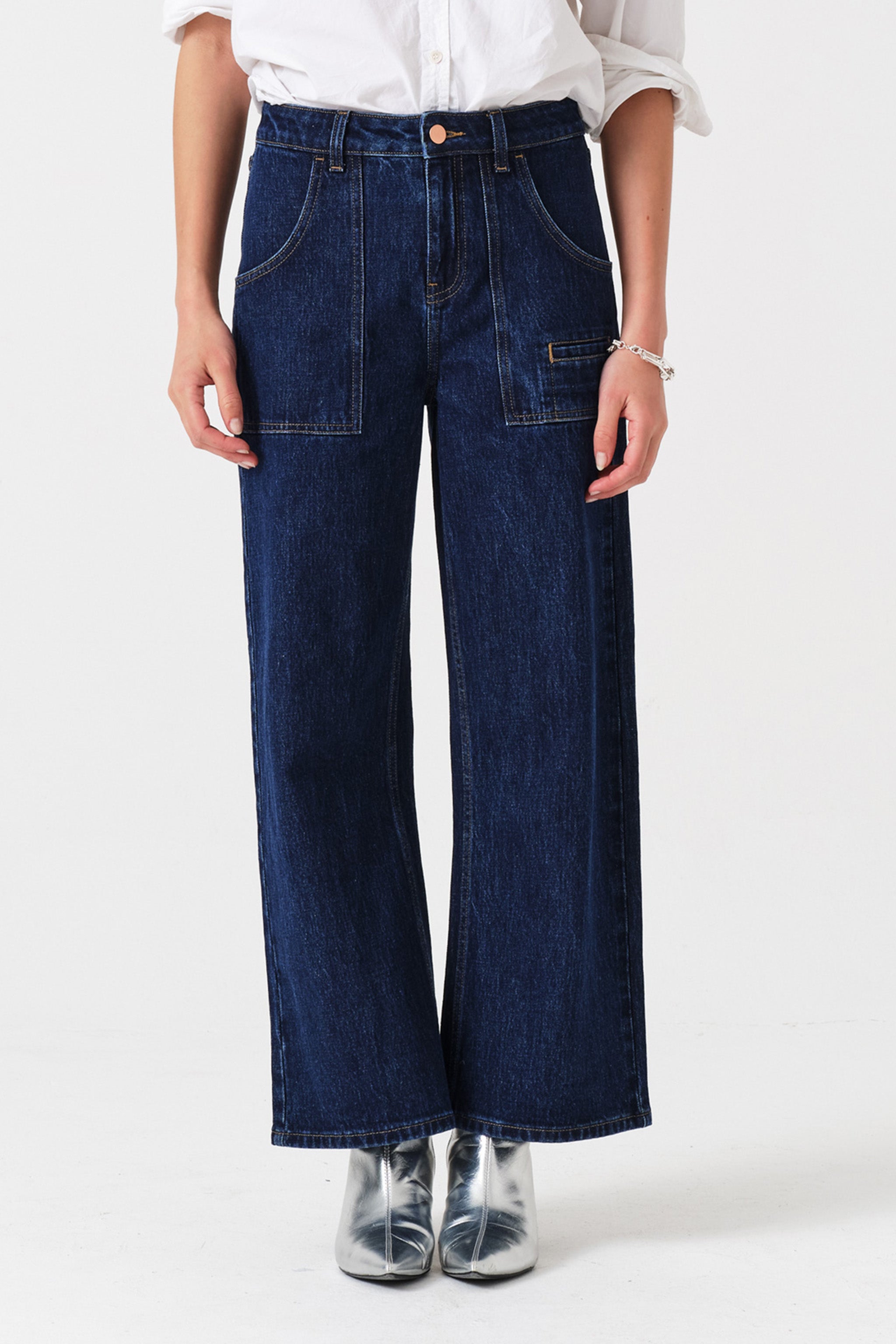 Woman wearing dark wash blue cropped wide-leg jeans with pocket details and a white shirt on a white background